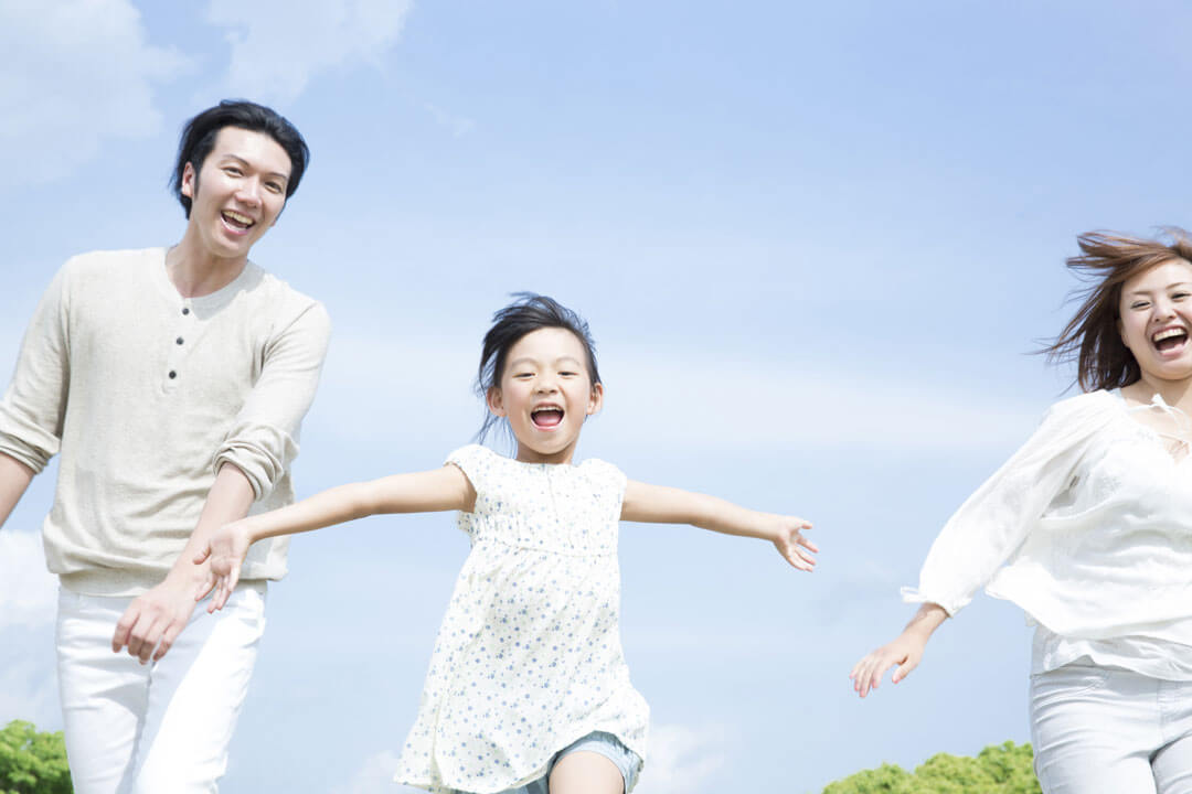 青空の下で両手を広げて走る女の子と両親