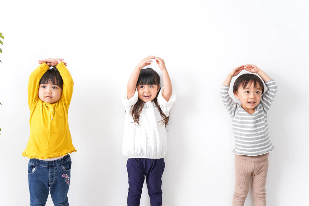 両手を上げて頭の上で丸を作る3人の子供