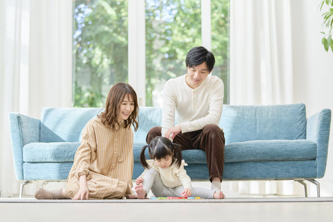 リビングのソファーの前で遊ぶ子供と見守る両親