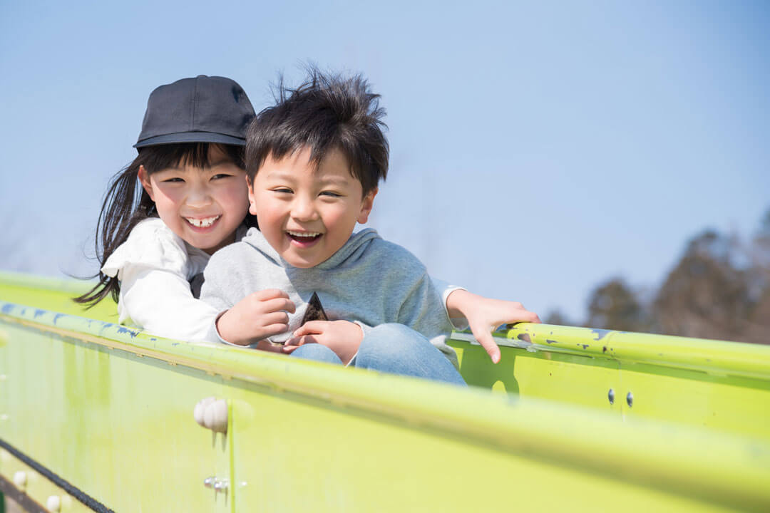 仲良く滑り台を滑る2人の子供