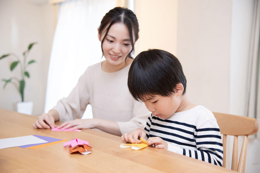 折り紙をする男の子と見守る母親